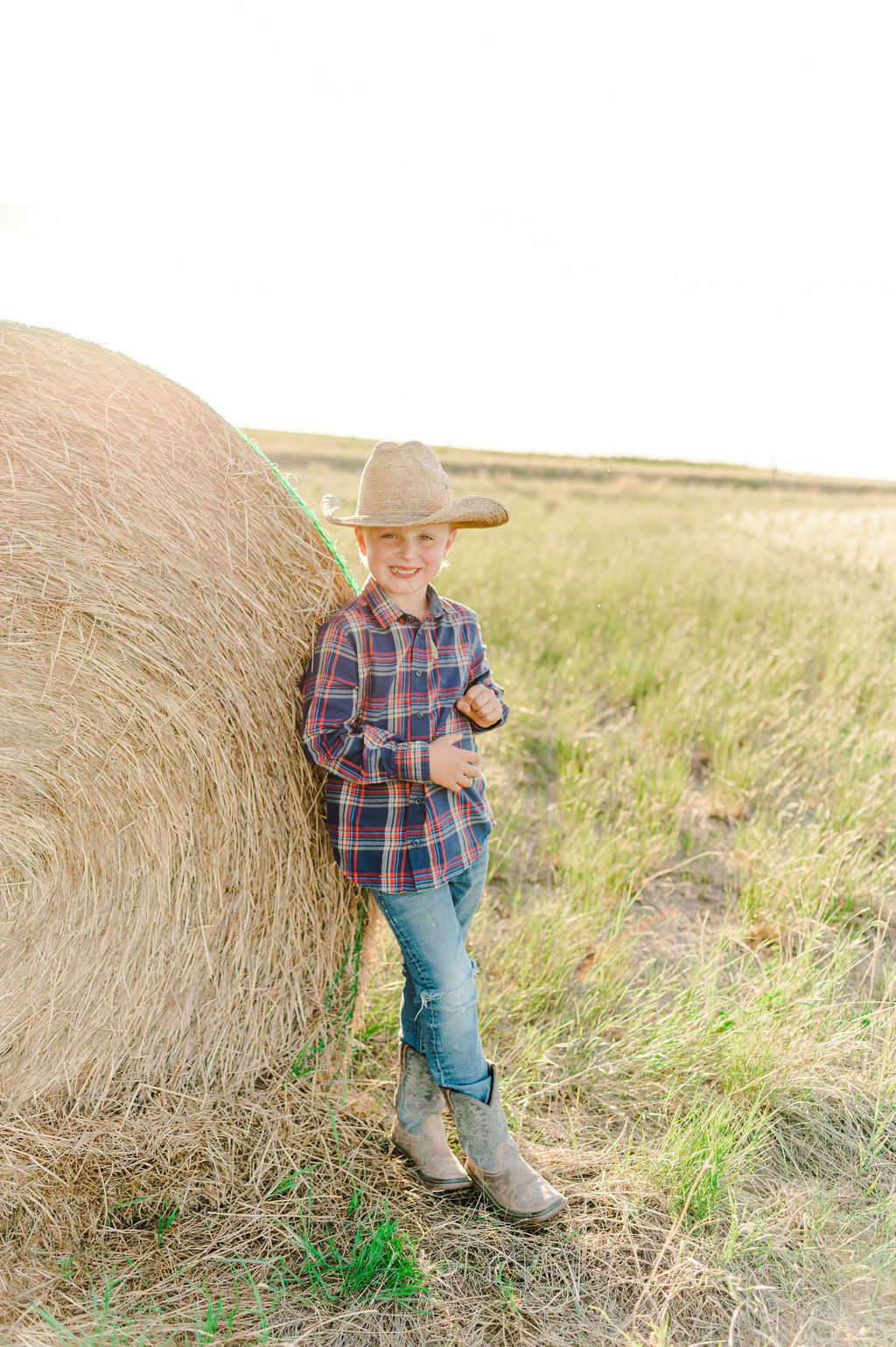 Boy with a cowboy hat standing next to a hay bale on stick leg ranch