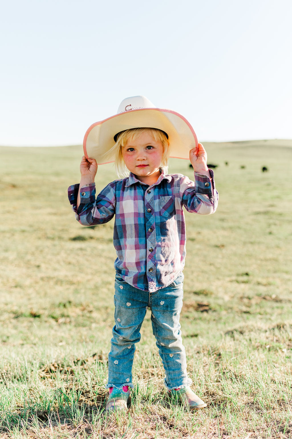 Little girl standing in the middle of a cow pasture with a cow boy hat on.
